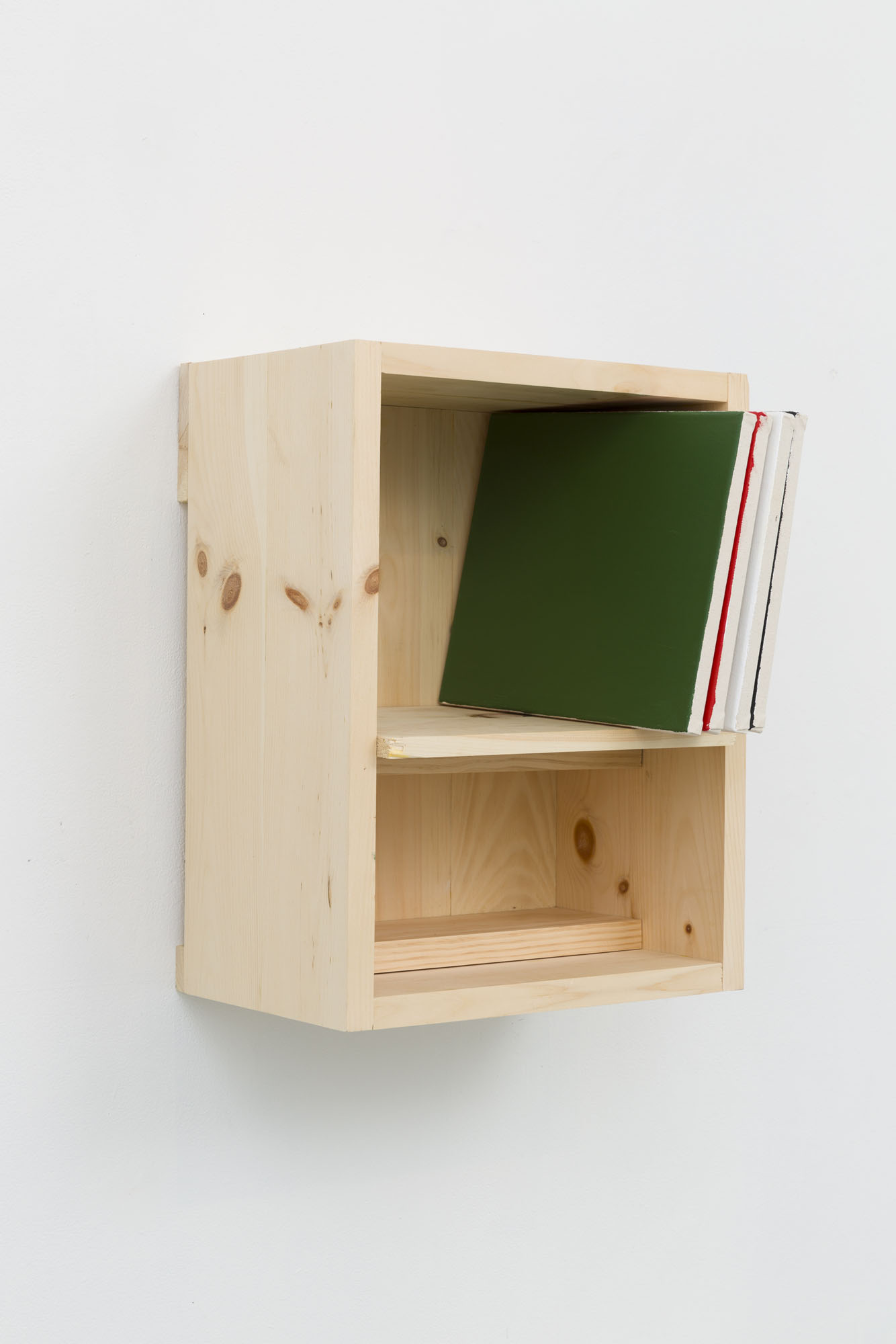 A pinewood box installed on the wall on its side has a shelf with four canvases stacked on their side with color field paintings in green, red, white and black.