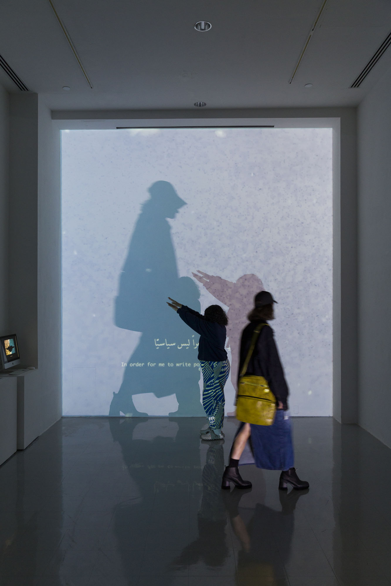 This projected video is set up with two monitors which create an interactive field in which when someone stands in front of one projector, the video content from the other projector is made clear. Saba stands with her arms outstretched in front of her, creating a shadow from one of the projectors as Quin walks by creating another shadow in front of the other projector.