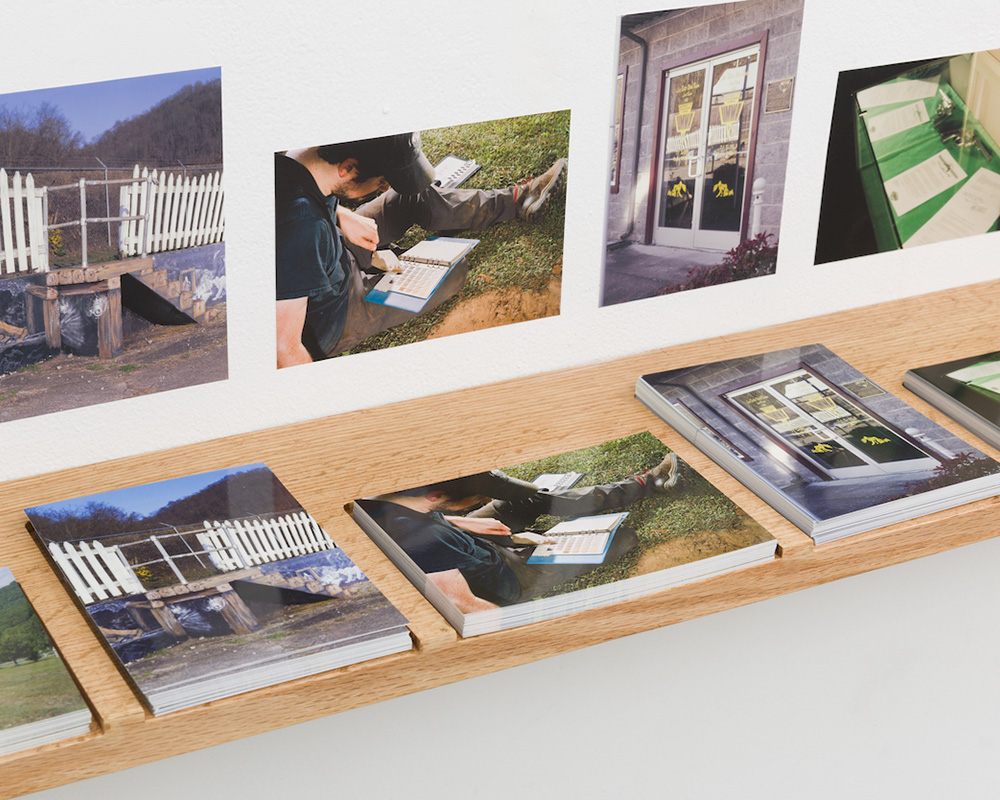 A close up image of a shelf holding a series of postcards. Each stack of postcards sits in a routed out slot, and on the wall above each postcard is a vinyl sticker of the image on the card itself.